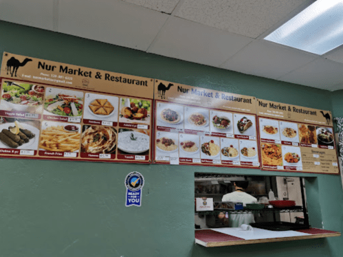 Menu board at Nur Market & Restaurant featuring various dishes like falafel, chicken, and vegetarian options.