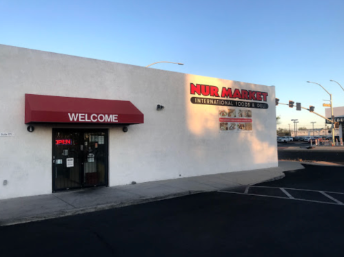Exterior of Nur Market, an international foods and deli store, featuring a red awning and "OPEN" sign.