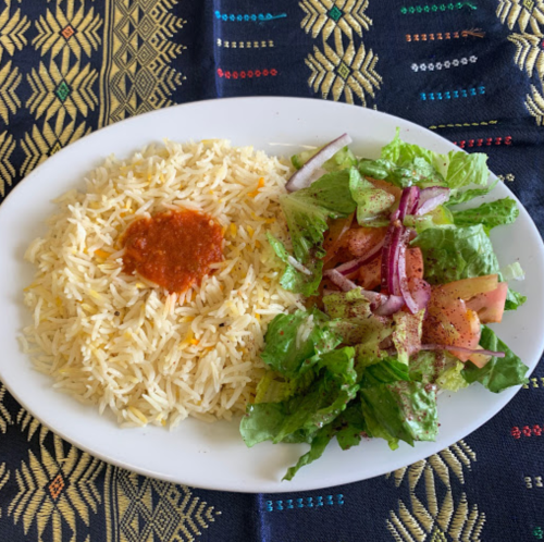 A plate of fluffy rice with a small portion of sauce, accompanied by a fresh salad of greens, tomatoes, and onions.