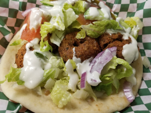 A pita filled with falafel, lettuce, tomatoes, onions, and drizzled with sauce, served on a checkered paper.