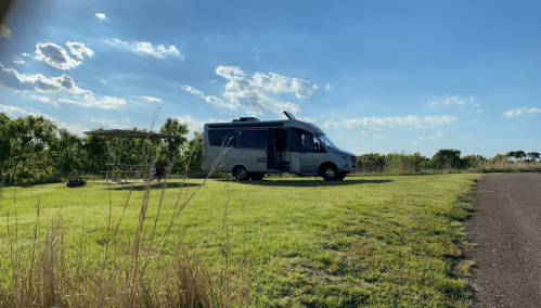 A camper van parked on a grassy area with a picnic table nearby, under a blue sky with scattered clouds.