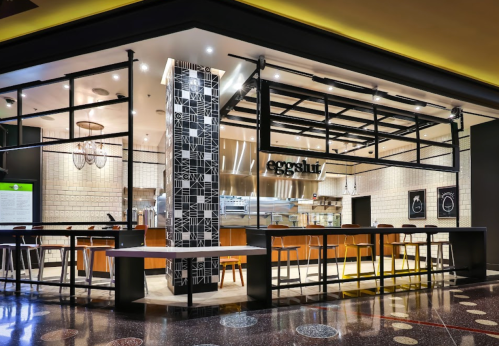 A modern restaurant exterior with a sleek design, featuring a black and white patterned wall and bar seating.