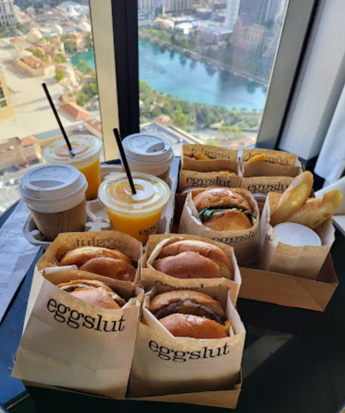 A table with Eggslut burgers and drinks, overlooking a scenic view of a city and water.