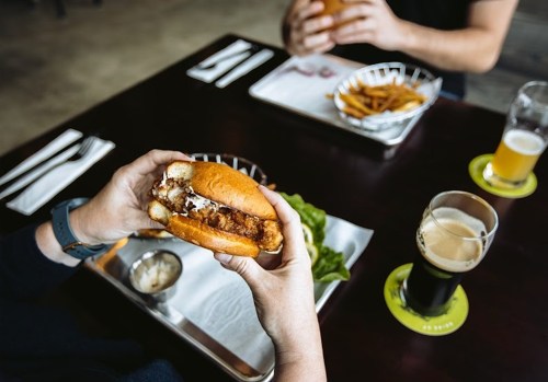 A person holds a crispy chicken sandwich with fries and drinks on a table in a casual dining setting.