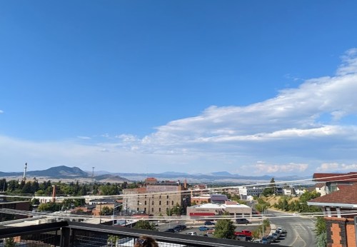 A panoramic view of a town with buildings, mountains, and a clear blue sky in the background.