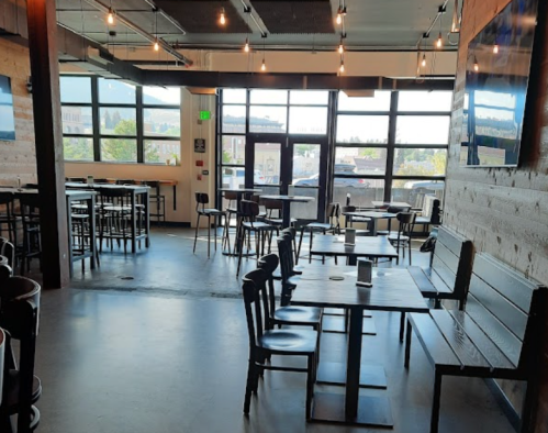 A spacious, modern restaurant interior with wooden accents, tables, and large windows letting in natural light.