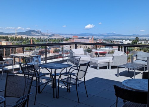 Rooftop terrace with seating and a panoramic view of mountains and cityscape under a clear blue sky.