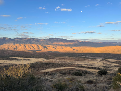 A scenic view of rolling mountains under a blue sky with scattered clouds and a hint of moonlight.