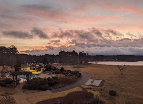 A serene lakeside view at sunset, featuring a pool area and lush landscaping under a colorful sky.