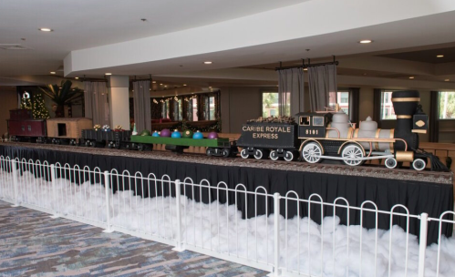 A decorative train display with colorful cars and a black engine, set on a table with a white cloud-like backdrop.