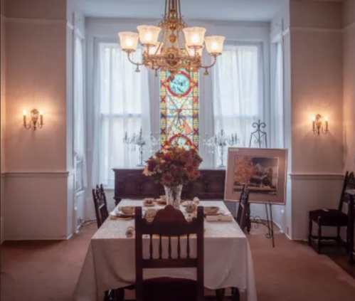 Elegant dining room with a chandelier, stained glass window, and a table set with flowers and dinnerware.