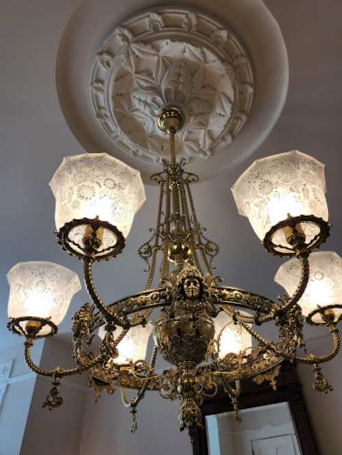 A decorative chandelier with ornate gold details and lace-patterned shades, hanging from a floral ceiling medallion.
