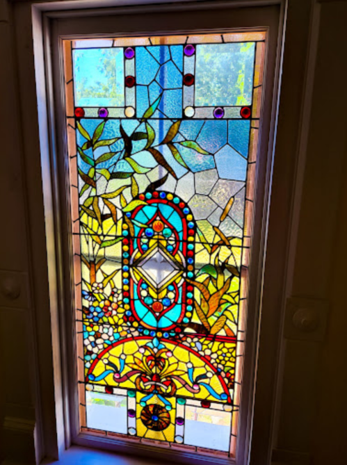 Colorful stained glass window featuring intricate floral and geometric designs. Natural light filters through.