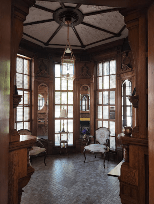 A vintage room with wooden walls, large windows, and elegant furniture, featuring intricate architectural details.