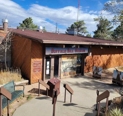 Exterior of the Buffalo Bill Museum, featuring wooden architecture and signage, surrounded by trees and blue sky.