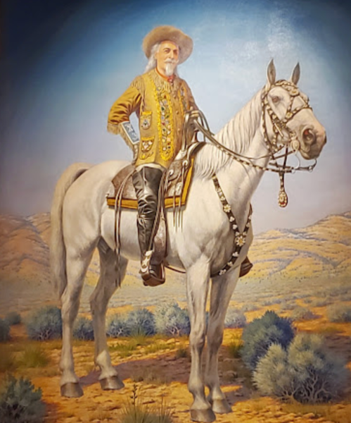 A man in a colorful outfit and hat rides a white horse against a desert landscape.