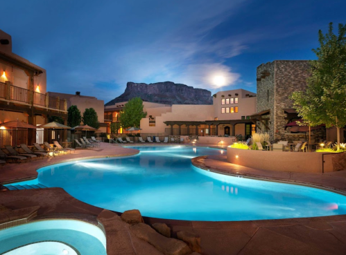 A serene pool area at dusk, surrounded by buildings and mountains, with lounge chairs and soft lighting.