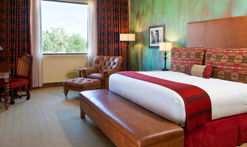 Cozy hotel room featuring a king bed, armchair, and colorful wall decor with a window view.