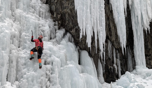 A climber ascends a frozen waterfall, surrounded by icicles and icy rock formations.