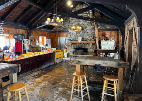 Cozy rustic interior of a shop with wooden beams, stone fireplace, and a counter displaying various products.