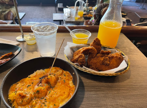A table setting with shrimp and grits, fried chicken, a glass of water, and a small cup of orange juice.