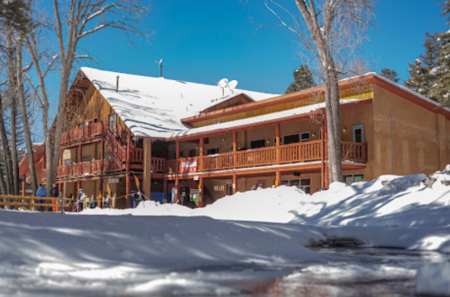 A snow-covered building with wooden balconies, surrounded by trees and a clear blue sky.