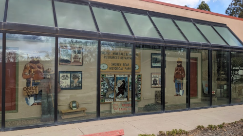 Exterior view of a building with large windows displaying Smokey Bear-themed posters and historical park information.