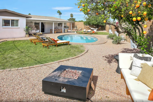 A sunny backyard with a pool, lounge chairs, a fire pit, and an orange tree, creating a relaxing outdoor space.