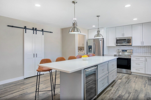 Modern kitchen featuring a large island, bar stools, stainless steel appliances, and light wood flooring.