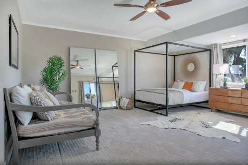 Spacious bedroom with a four-poster bed, seating area, large mirror, and natural light from windows.
