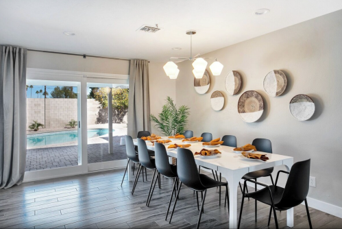 A modern dining room with a long white table, black chairs, and decorative wall plates, overlooking a pool area.