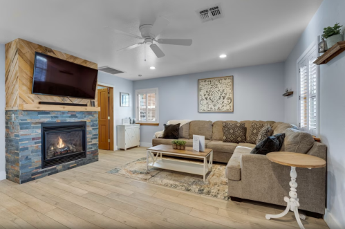 Cozy living room with a stone fireplace, large sectional sofa, and a mounted TV on a wooden accent wall.