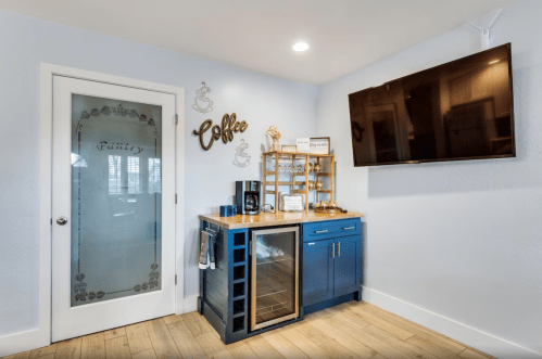 A cozy coffee station with a blue cabinet, mini fridge, and a TV on the wall, next to a decorative pantry door.