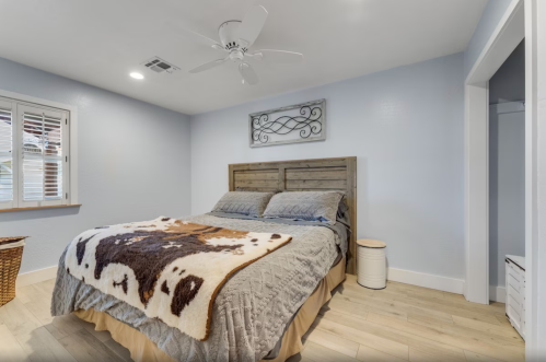 Cozy bedroom with a wooden bed, gray bedding, a decorative wall piece, and light blue walls.