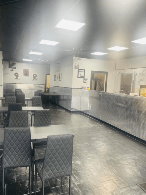 Interior of a modern restaurant featuring black tables, quilted chairs, and a shiny silver counter.