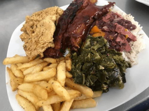 A plate of food featuring fried chicken, ribs, rice with beans, collard greens, and French fries.