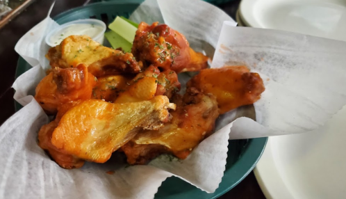 A plate of buffalo chicken wings garnished with parsley, served with celery sticks and a side of dipping sauce.
