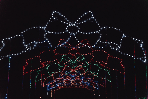 Colorful holiday lights in the shape of bows and flowers create a festive archway against a dark background.