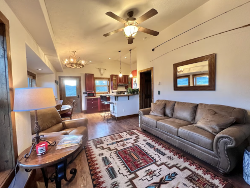 Cozy living room with a brown sofa, patterned rug, and open kitchen, featuring wooden accents and natural light.