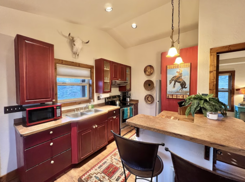 Cozy kitchen with red cabinets, a bar area, and rustic decor, featuring a microwave and a view of the outdoors.