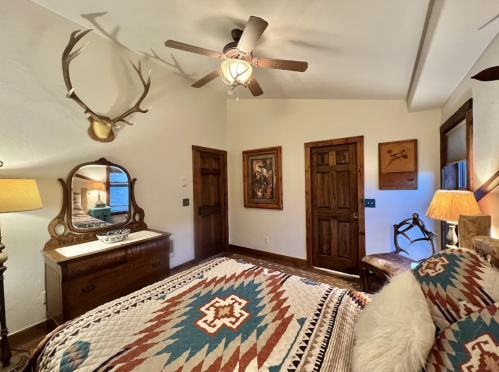 Cozy bedroom with rustic decor, featuring a patterned quilt, wooden furniture, and antler accents on the wall.