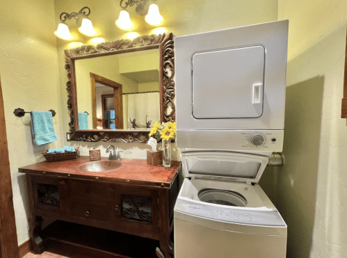 A cozy bathroom featuring a wooden vanity, a large mirror, and a stacked washer and dryer beside it.