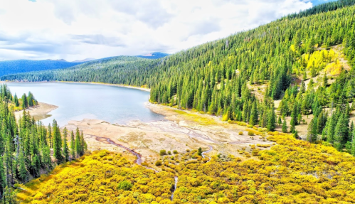 A serene lake surrounded by lush green forests and vibrant autumn foliage under a cloudy sky.