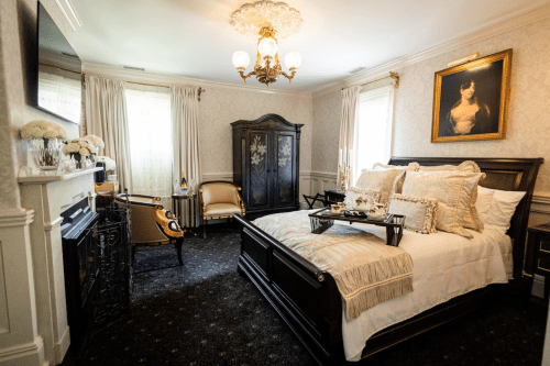 Elegant bedroom featuring a large bed, vintage furniture, a fireplace, and a classic painting on the wall.