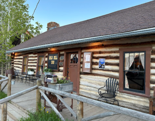 A rustic log cabin with a porch, featuring a sign that reads "Old Town Inn" and surrounded by greenery.