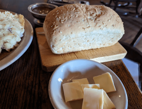 A loaf of bread on a wooden board, with a small dish of butter squares and a side of gravy.