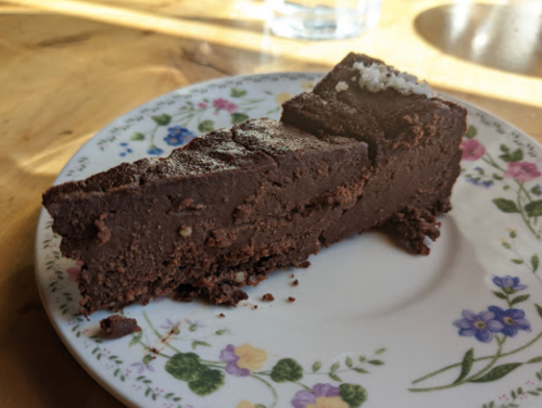 A slice of rich chocolate cake on a floral-patterned plate, with a light dusting of powdered sugar on top.