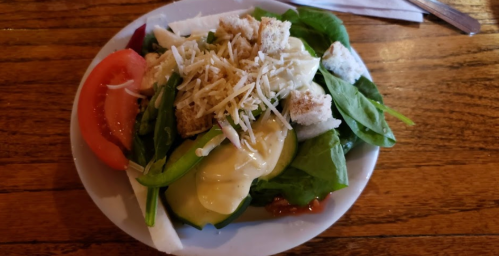 A fresh salad with spinach, tomato, cucumber, croutons, and shredded cheese, drizzled with dressing on a white plate.