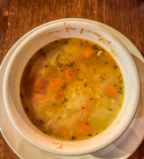 A bowl of soup with vegetables, including carrots and herbs, on a wooden table.