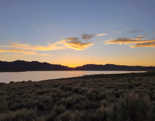 Sunset over a calm lake, with mountains in the background and a sky filled with soft clouds and warm colors.